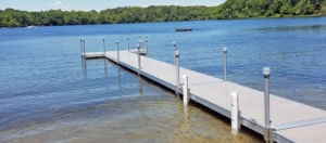 An aluminum dock with composite decking extending over the water, held in place by tall aluminum pilings driven into the sand below.