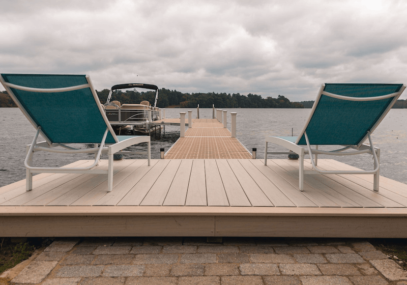 A-simple-L-shaped-dock-on-a-lake-with-a-small-boat-docked.-Two-lounge-chairs-are-placed-facing-the-water.