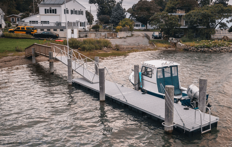 A-small-floating-dock-is-attached-to-large-wooden-pylons,-while-an-aluminum-gangplank-connects-the-dock-to-a-wooden-ramp.-A-small-fishing-boat-is-docked-alongside.