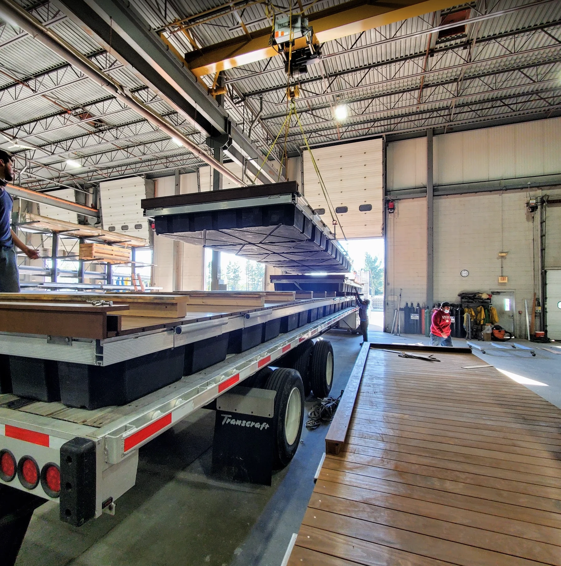 An overhead crane lifts a floating dock section onto a trailer inside the FWM factory.